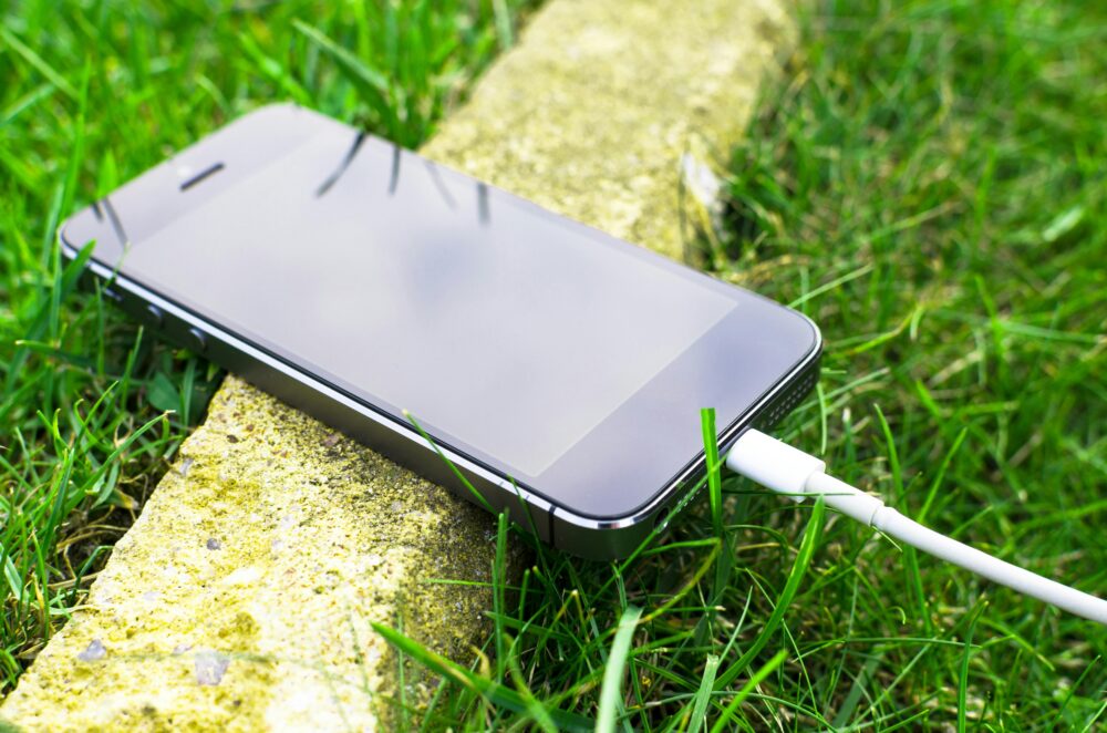 A smartphone with a charging cable rests on grass outdoors, showcasing modern technology in nature.