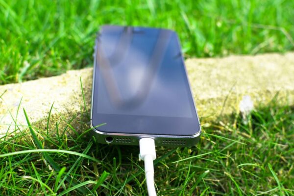 Close-up of a smartphone charging on a grassy lawn, highlighting modern technology in nature.
