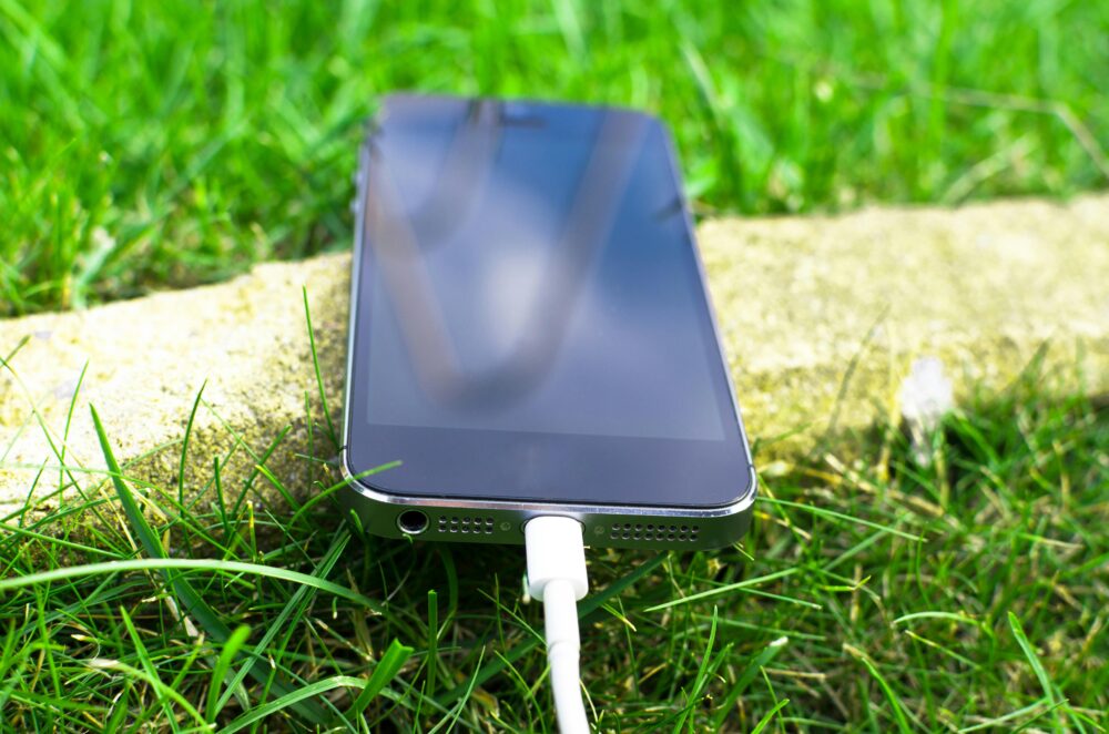 Close-up of a smartphone charging on a grassy lawn, highlighting modern technology in nature.