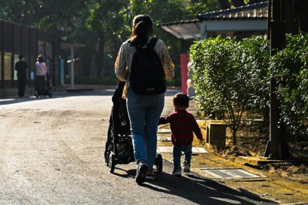 A mother and child stroll down a sunlit path, surrounded by greenery in Kaohsiung City, Taiwan.
