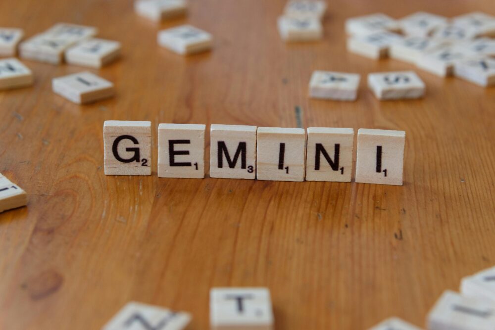 Gemini zodiac sign spelled with Scrabble tiles on a wooden table.