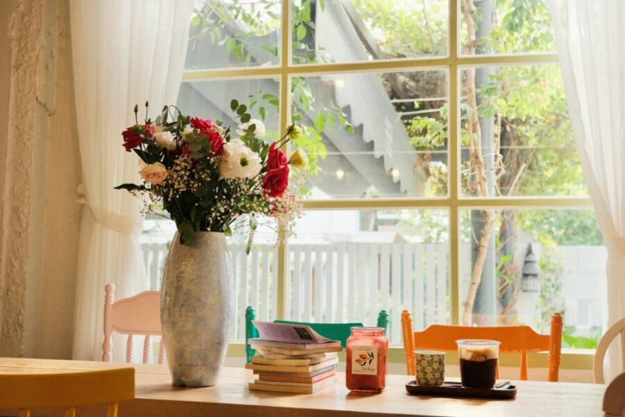 Cozy cafe table with flowers, books, and drinks by a bright window.