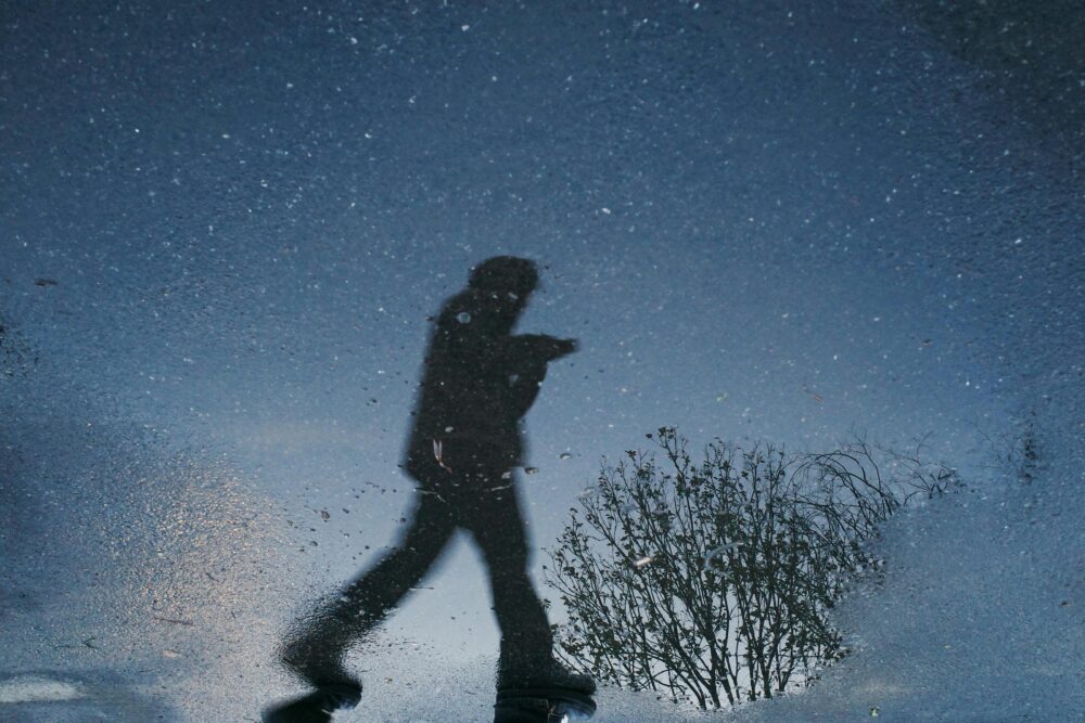 Silhouette of a walking person reflected in a puddle on a starry night