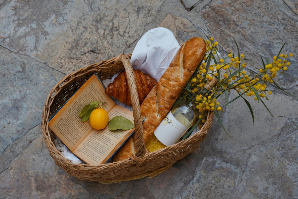 Charming picnic basket with a baguette, croissant, book, lemon, and mimosa flowers.