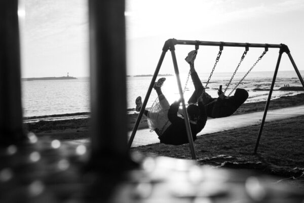 A couple enjoys swinging together by the seaside, capturing joyful moments in black and white