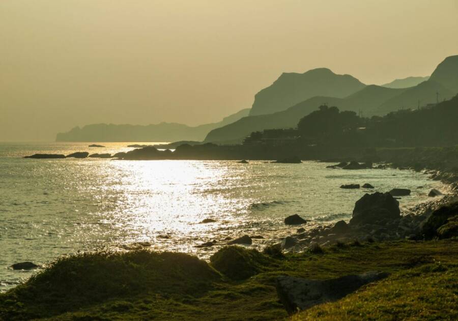 Peaceful sunrise over the rugged coastline of New Taipei City, Taiwan, reflecting golden hues.
