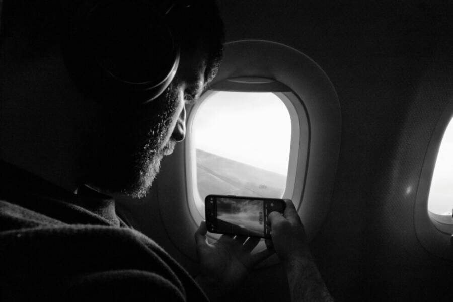 Man taking photo out of airplane window, capturing wing view with smartphone
