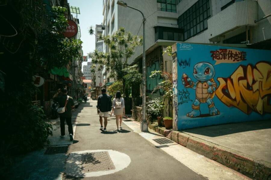 A vibrant Taiwanese street with people walking past a colorful graffiti wall during the day