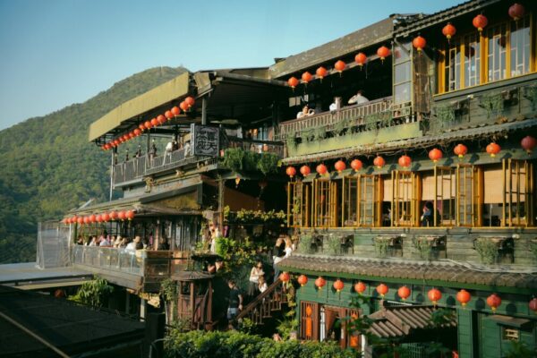 Traditional Jiufen tea house adorned with red lanterns, beautifully lit at sunset, surrounded by lush mountains.
