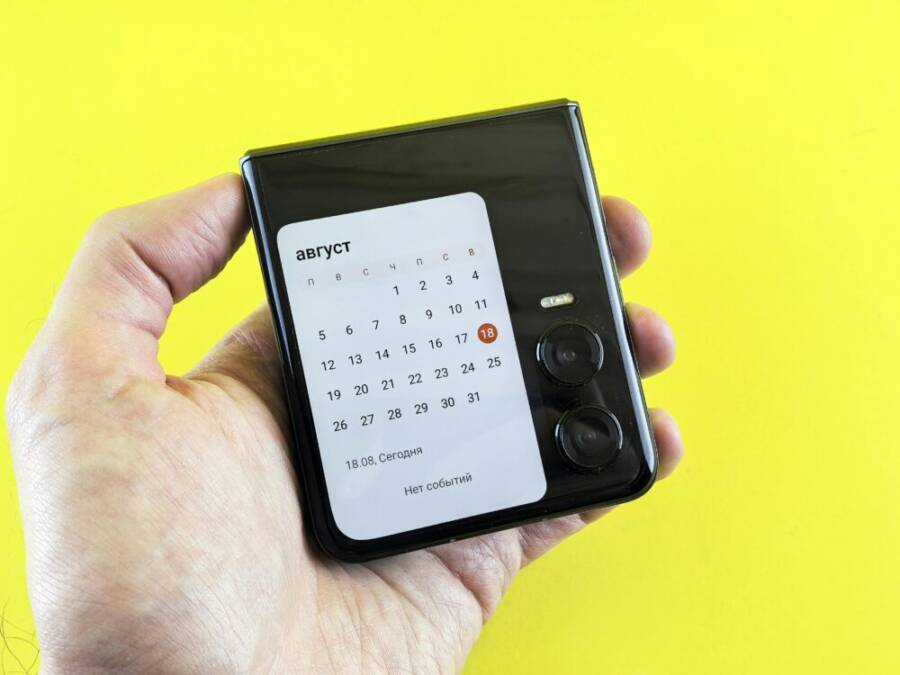 Close-up of a hand holding a compact smartphone with a calendar on screen against a vibrant yellow background