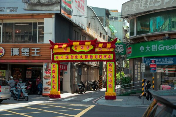 A vibrant traditional archway with colorful decorations on a bustling Taipei street.