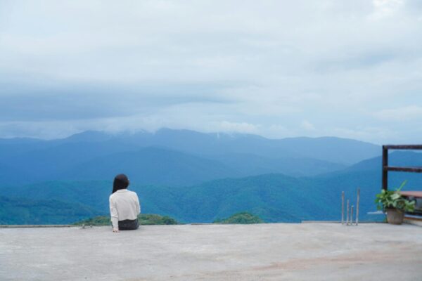 Woman sitting alone, contemplating the expansive mountain landscape for a serene moment.