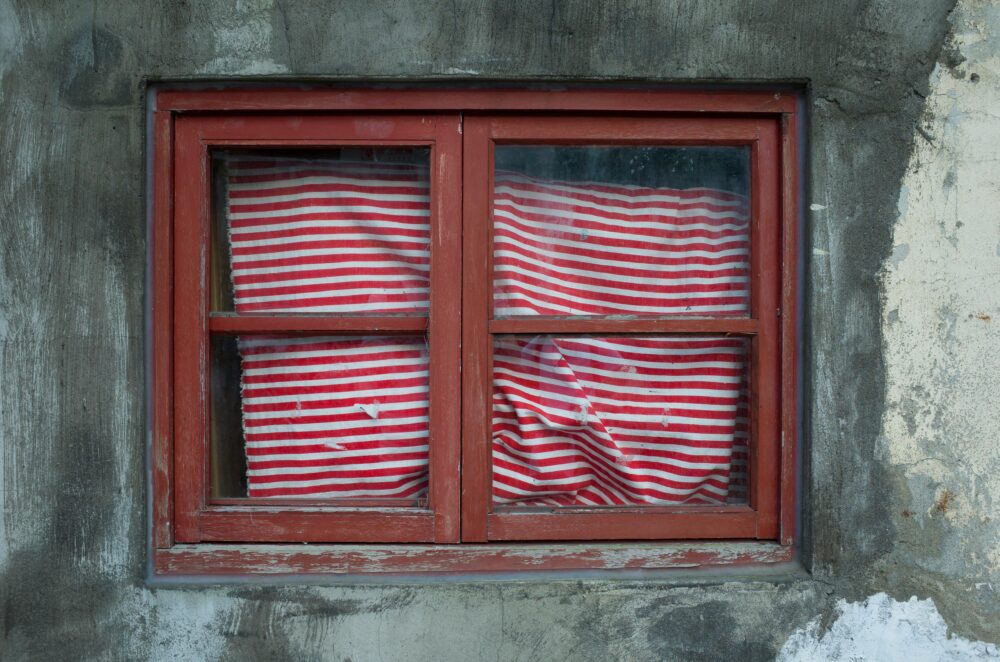A weathered red-framed window with a red and white striped curtain on a concrete wall in Taipei, Taiwan.