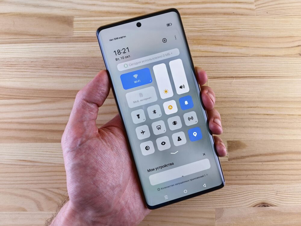 A hand holding a smartphone displaying the control center against a wooden backdrop.