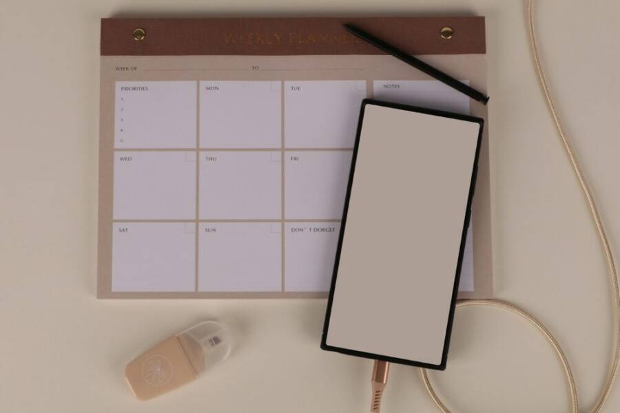 Flat lay of a minimalist desk setup featuring a weekly planner, smartphone, and stationery