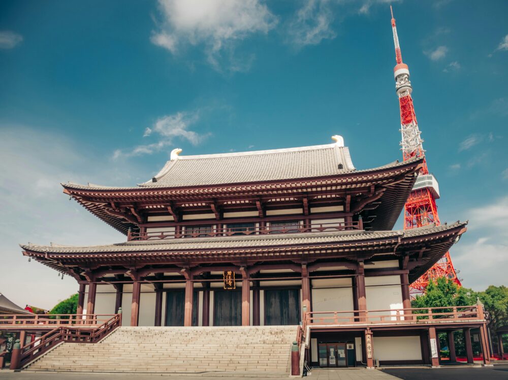 Beautiful summer view of Tokyo Tower behind the historic Zojoji Temple under a clear blue sky.