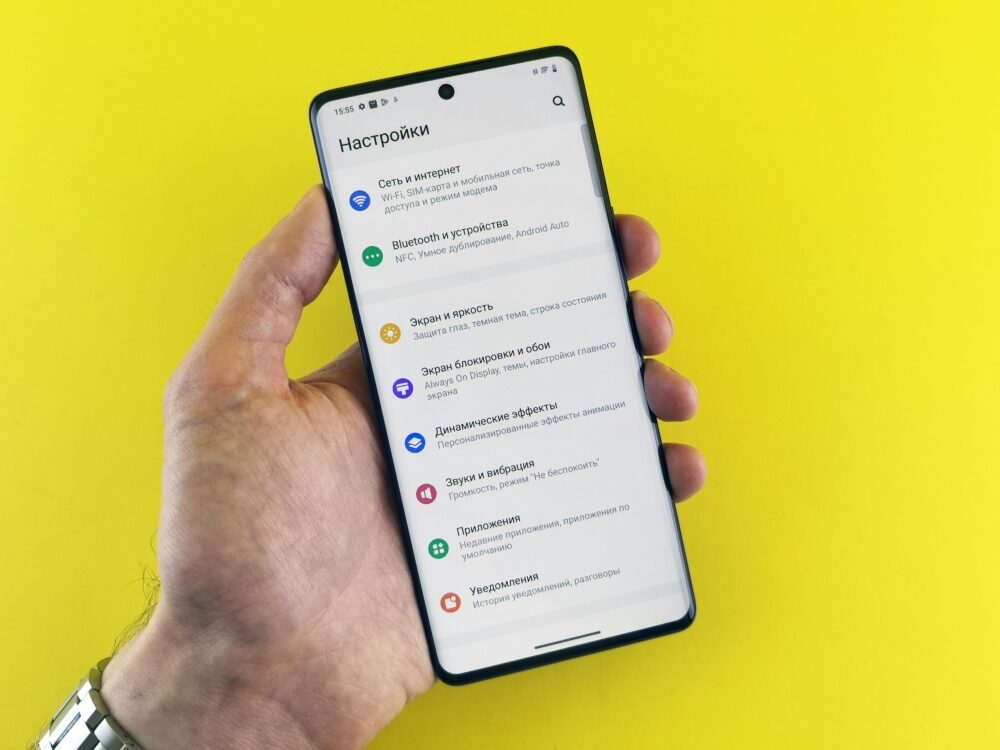 Close-up of a hand holding a smartphone with settings menu on a bright yellow background