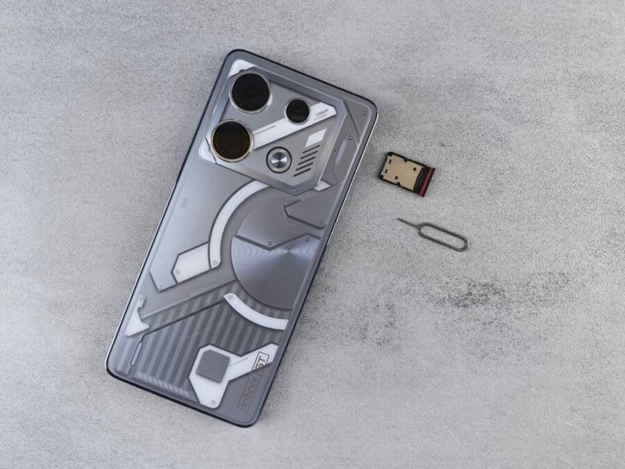 Close-up of a smartphone with futuristic design alongside a SIM card and ejector tool on a gray surface
