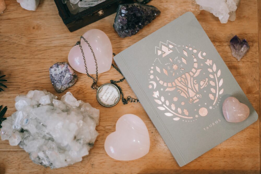 Taurus-themed notebook surrounded by heart-shaped and raw crystals on a wooden surface, evoking tranquility.
