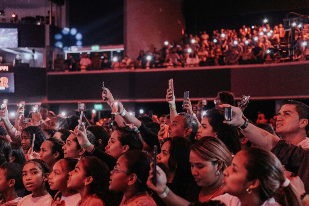 Lively audience enjoying a concert, capturing moments with smartphones in a vibrant atmosphere.