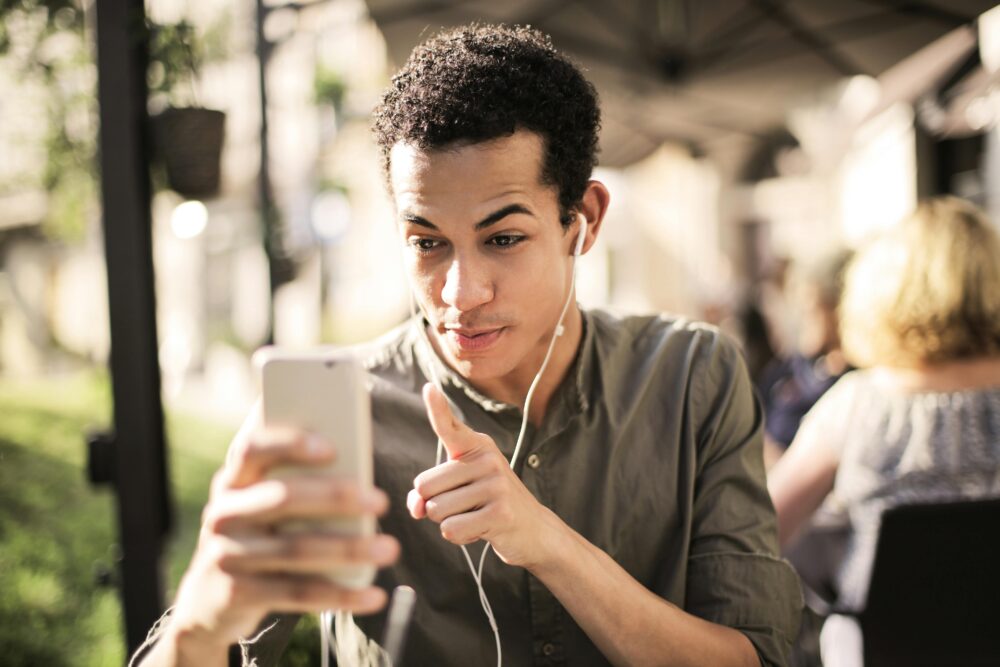 Young man wearing headphones, engaging in a video call outdoors on a sunny day.