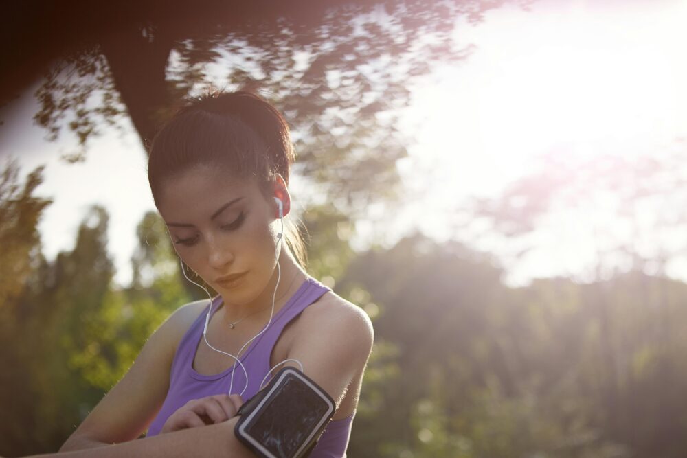 A young woman jogger enjoying music outdoors, wearing sportswear and a smartphone armband