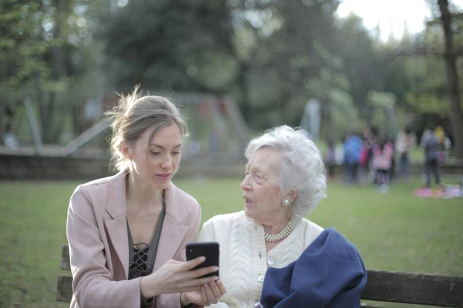 A) A young woman helps an elderly lady navigate a smartphone in a park, showcasing connection and support.