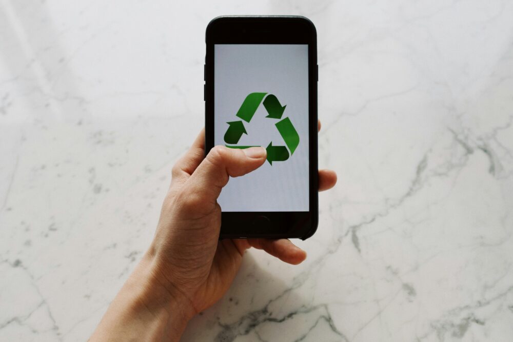 Hand holding smartphone displaying recycling symbol, promoting eco-friendly technology