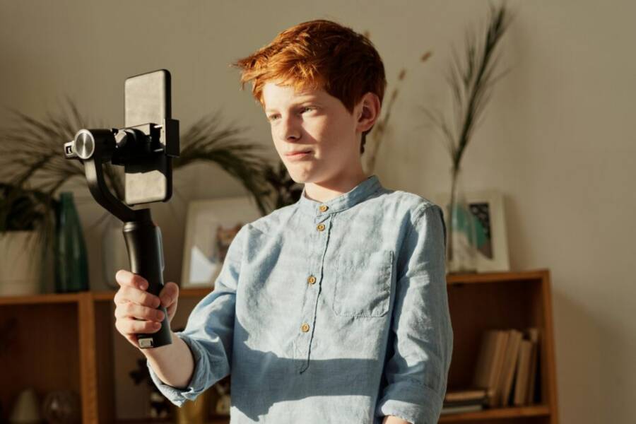 Young boy with red hair using a smartphone on a gimbal indoors, recording video.