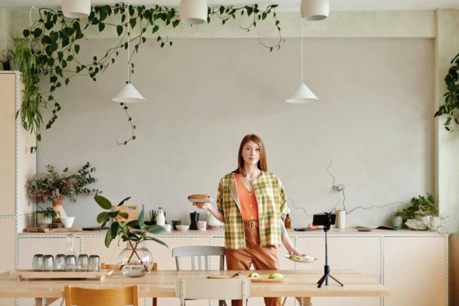 Woman in a modern kitchen setting up a vlog with a smartphone and tripod