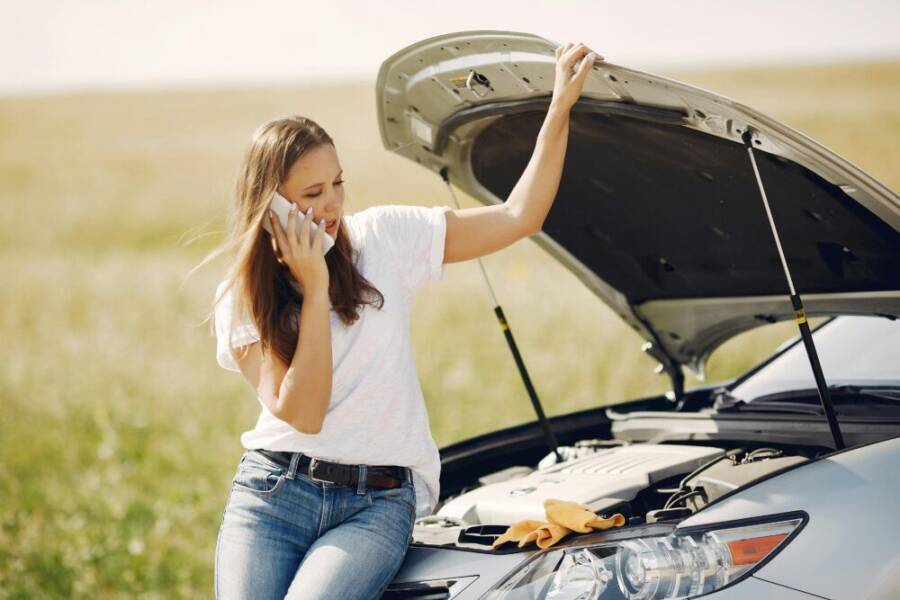 Young woman on phone seeking help for car breakdown on a sunny day