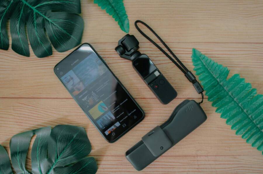 A flat lay of a smartphone and camera with green leaves on a wooden table