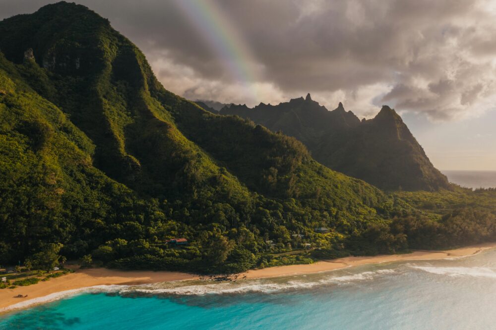 Idyllic view of lush mountains, vibrant sea, and a rainbow over a Hawaiian beach.