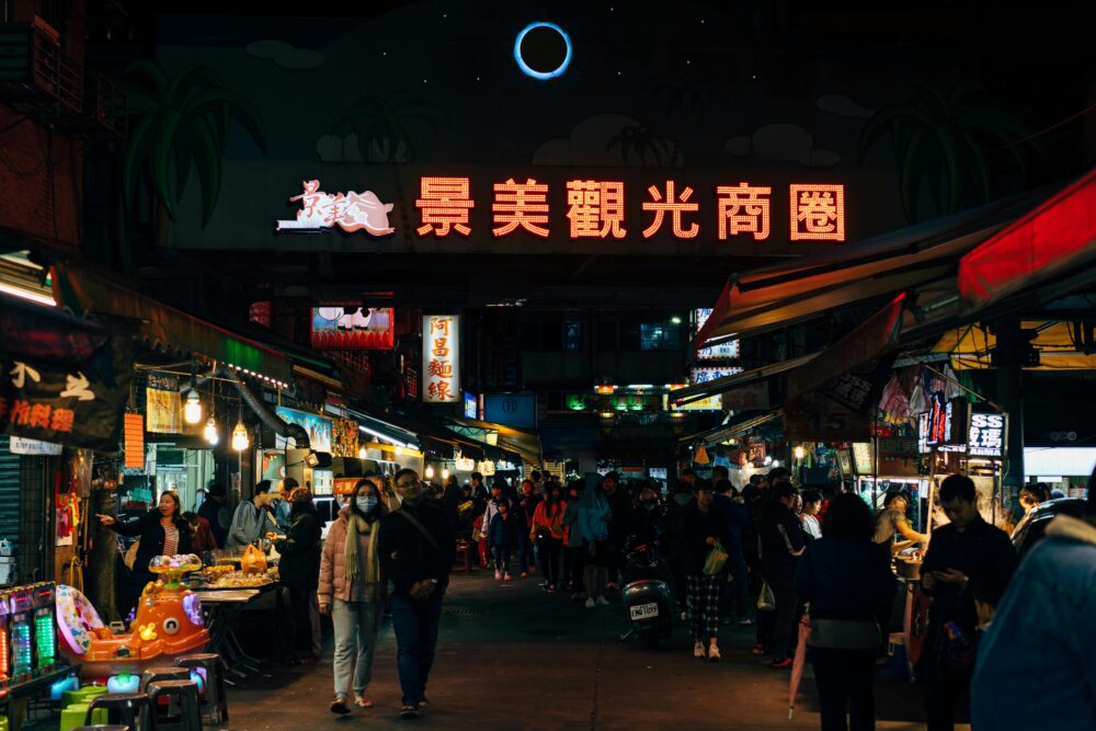 Vibrant scene of a busy night market in Taipei with bright lights and crowds.