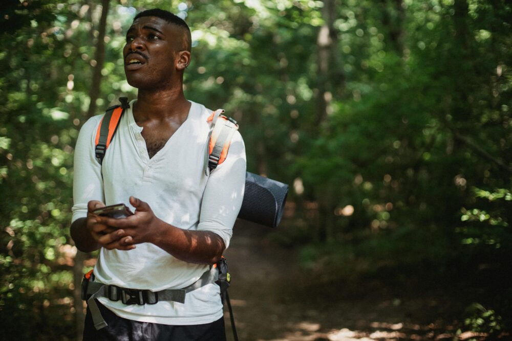 A hiker looks frustrated while using a smartphone to navigate in a dense forest