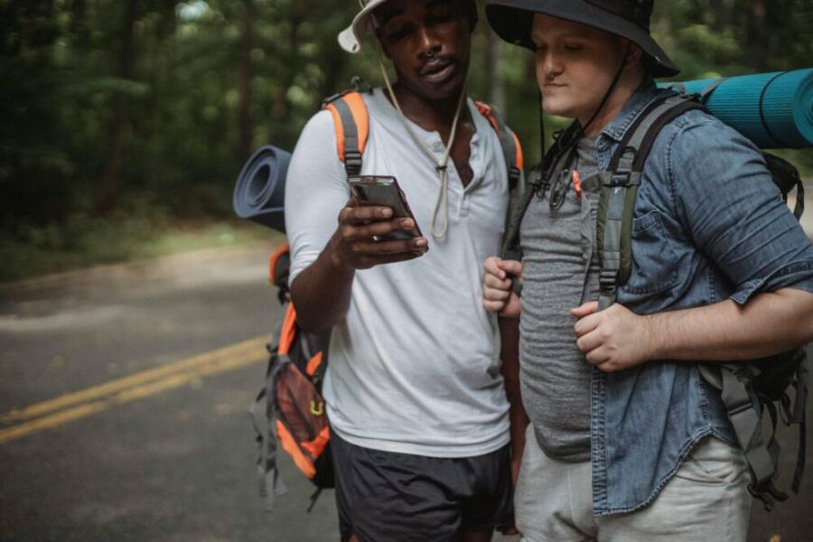 Two men hiking through a forest road, using a smartphone to navigate their adventure.