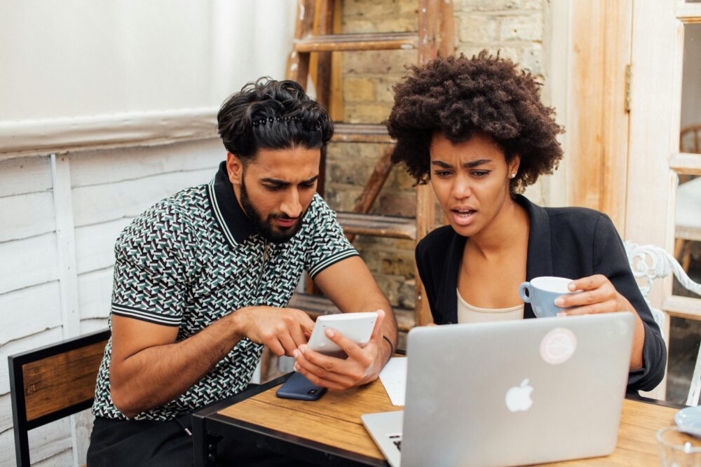 Two colleagues intensely working together with a laptop and phone, expressing surprise.