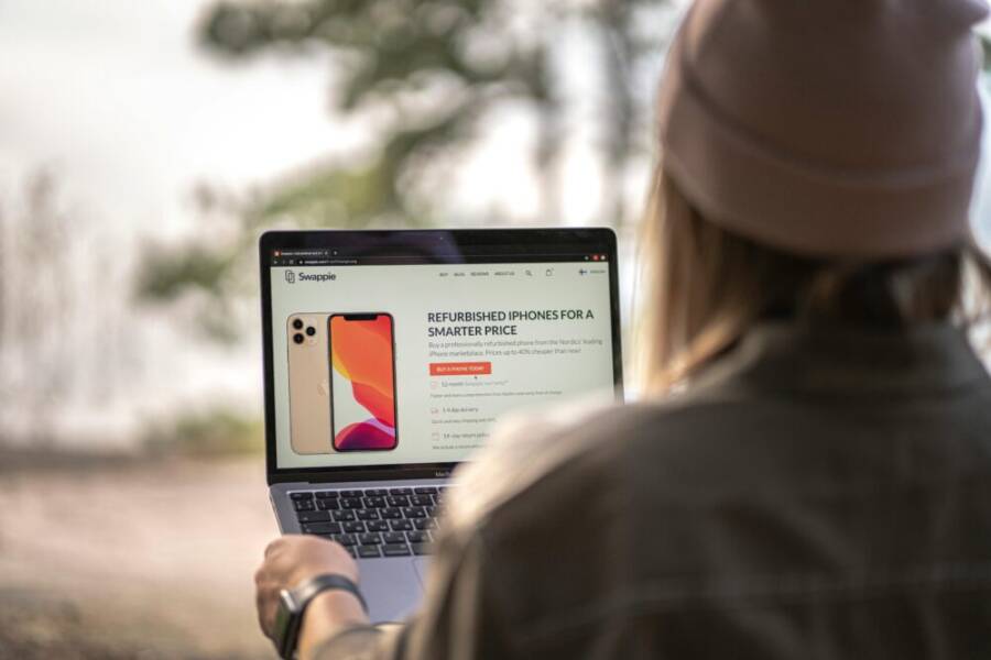 A woman using a laptop outdoors in Helsinki, Finland, viewing refurbished phone options