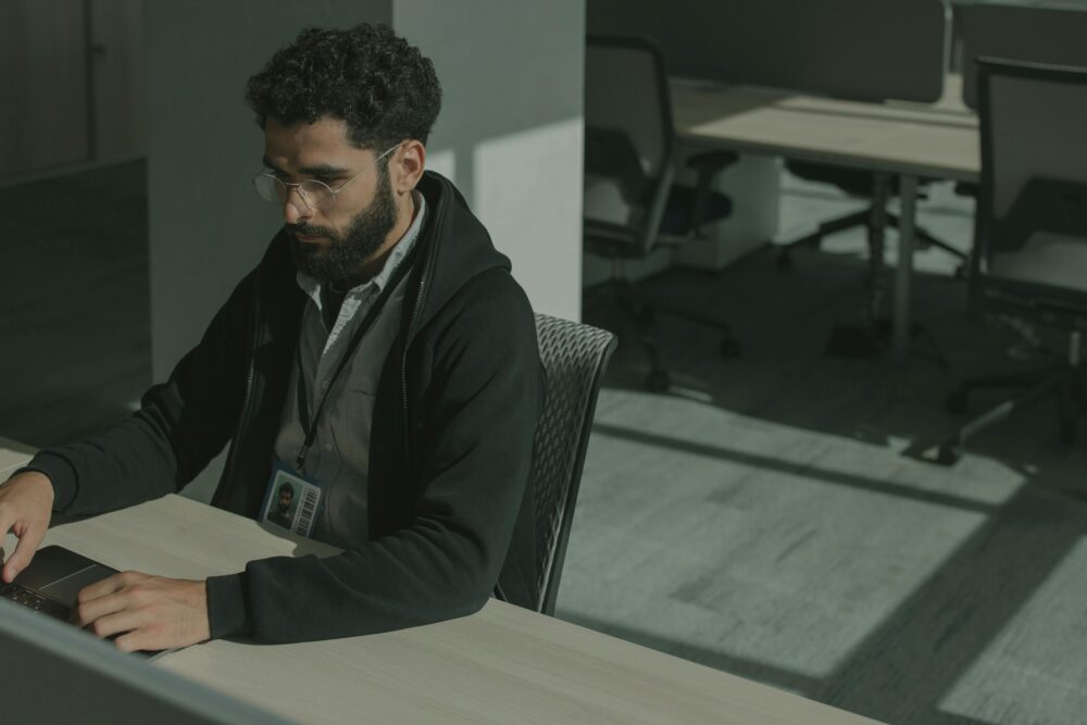 Bearded man working on a computer indoors, focused on cybersecurity tasks.