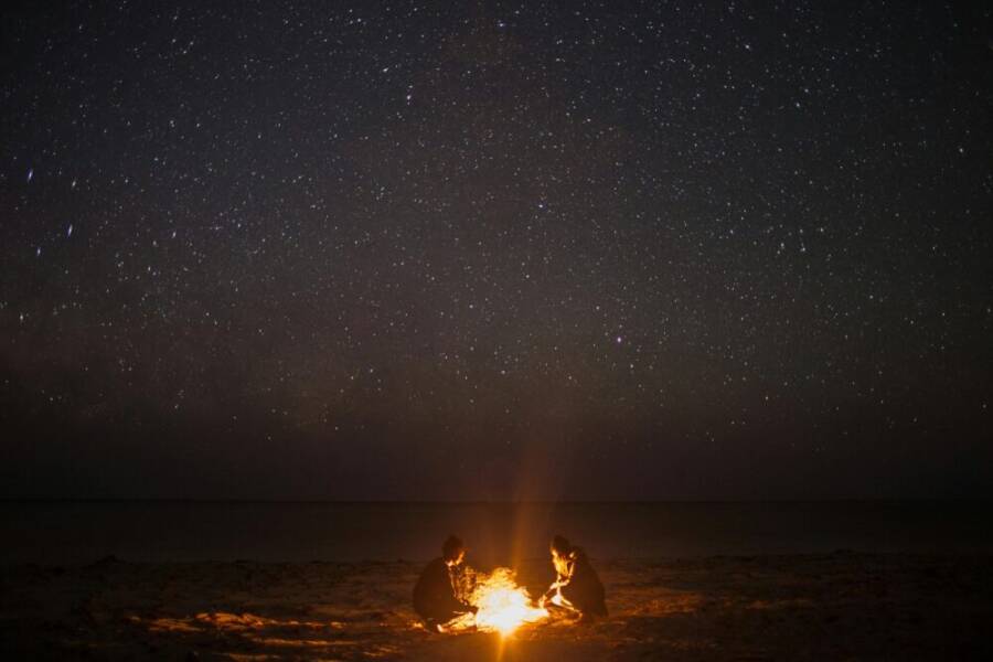 A couple enjoying a bonfire on a serene beach under a starlit sky