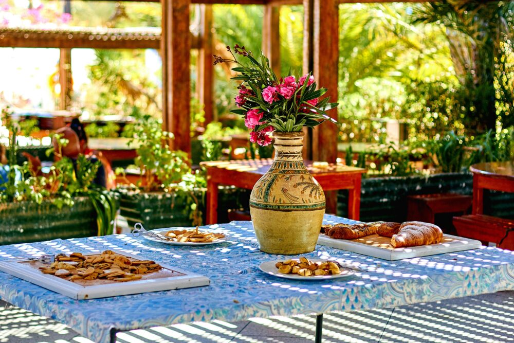 An inviting outdoor café table set with pastries and a decorative vase of flowers in a sunny setting