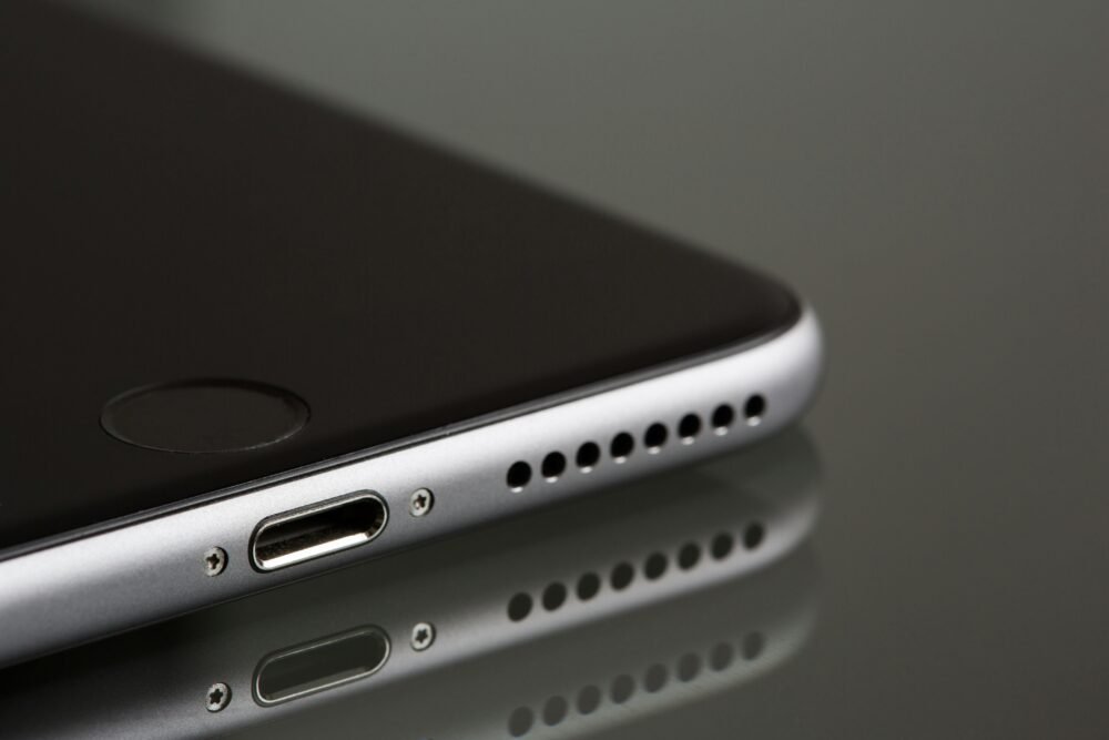A sleek smartphone close-up highlighting its lightning connector and speaker, reflecting on a surface