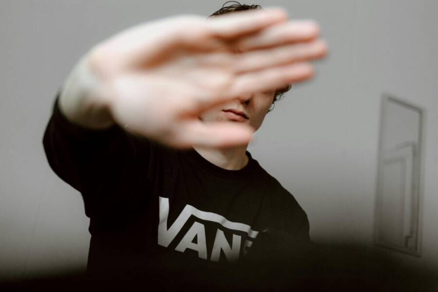 Young man indoors with hand covering face, creating a contemporary and casual mood.