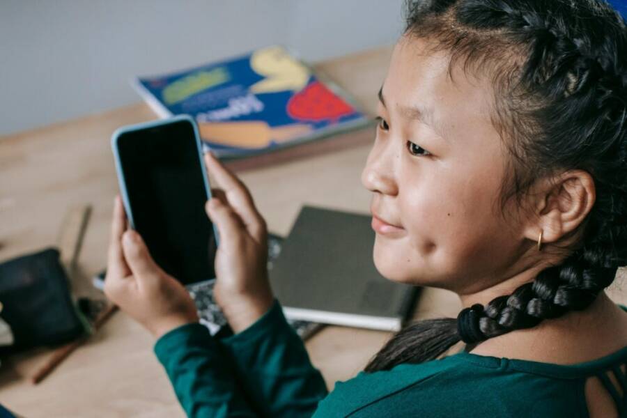 A cheerful girl in braids using a smartphone at her desk, exemplifying modern education and connectivity