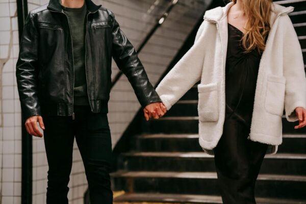 A couple in warm outerwear holding hands on a subway staircase, emphasizing affection.