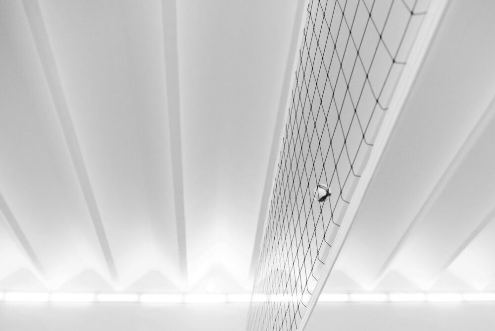 A modern minimalist shot of a volleyball and net indoors, emphasizing geometric patterns and soft lighting