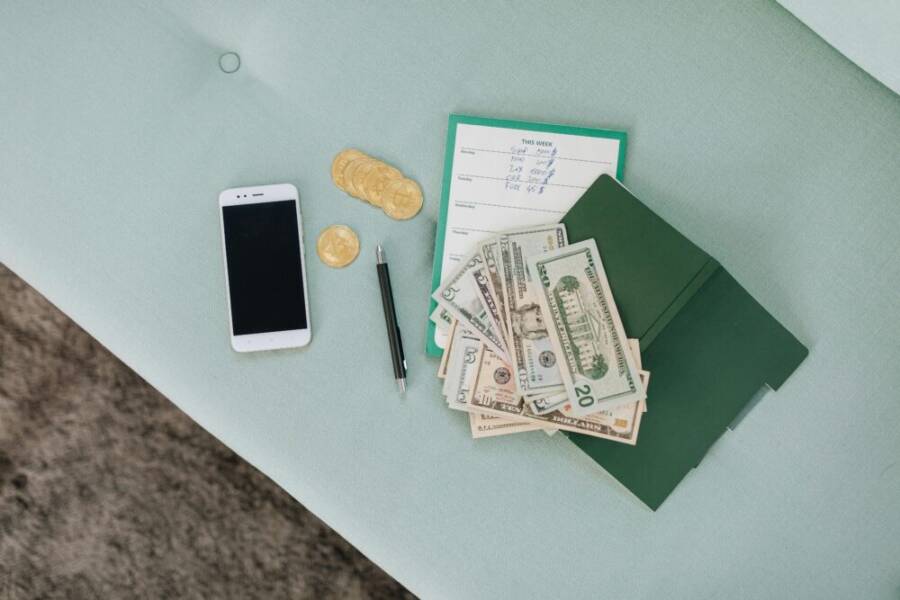 Flat lay of a smartphone, US dollar bills, coins, and a planner on a green surface
