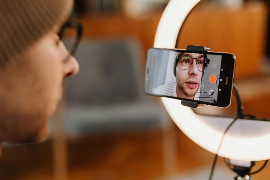 Close-up of a man recording a video with a smartphone and ring light indoors