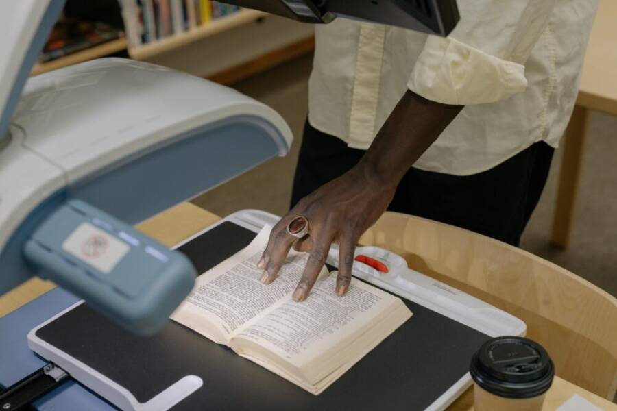 An anonymous individual scans a book in a library setting, emphasizing technology and research