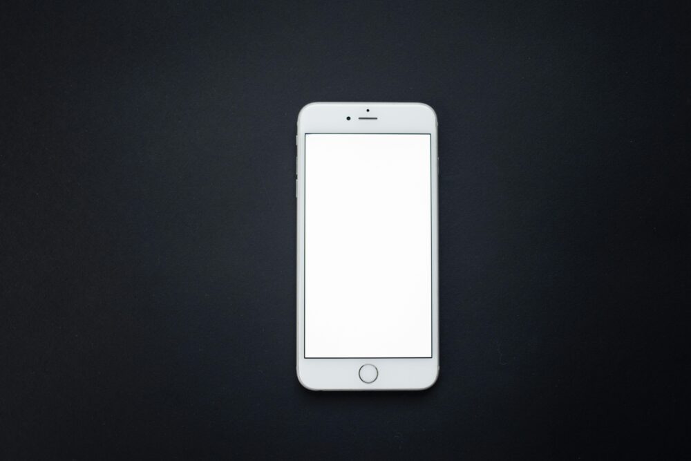 Flat lay of a blank smartphone screen on a dark surface, perfect for mockups and design presentations.